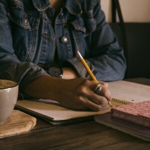 person writing in journal with coffee cup